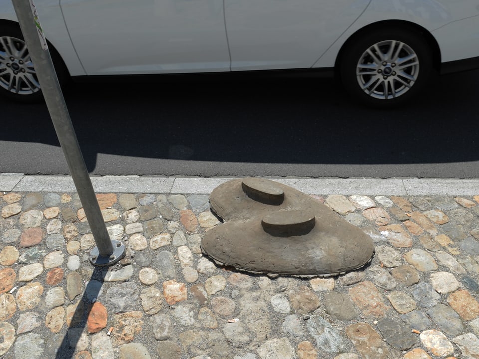 Auf dem Trottoir liegt ein herzförmiges Objekt aus Beton aus dem zwei runde Erhebungen ragen.