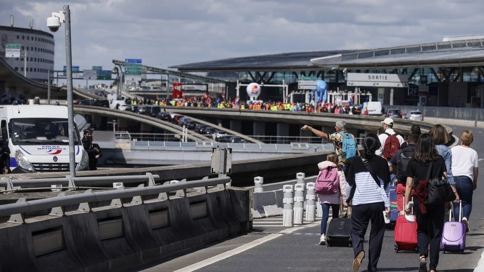 Personen stossen ihr Gepäck auf der Vorfahrtstrasse des Pariser Flughafens
