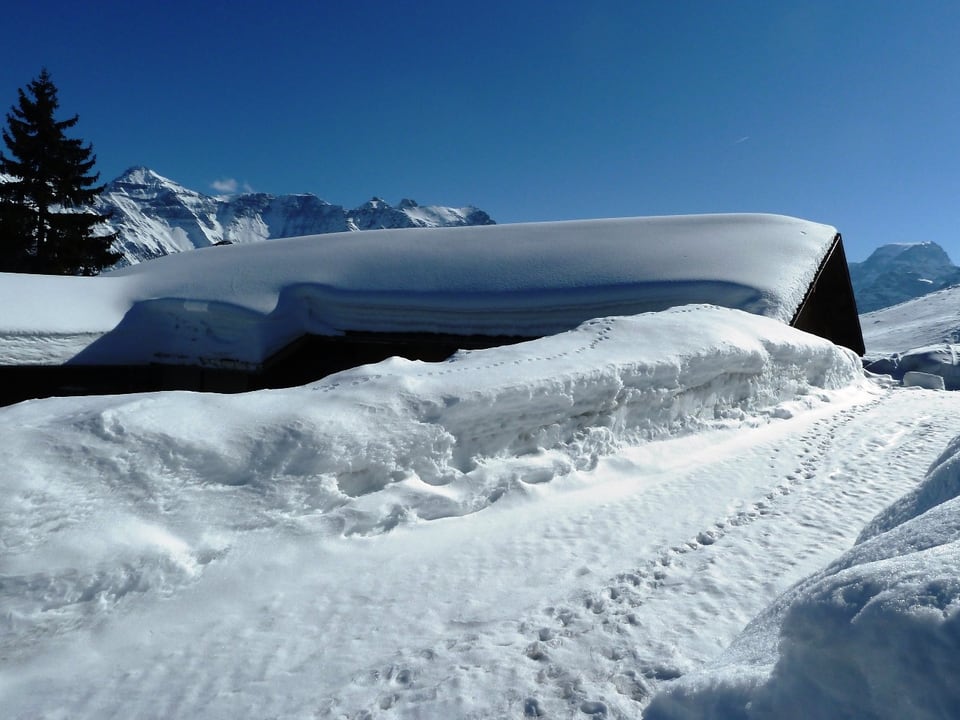 Das Hüttendach ist schwer mit Schnee beladen. Über dem Bergpanorama ist keine einzige Wolke auszumachen. 