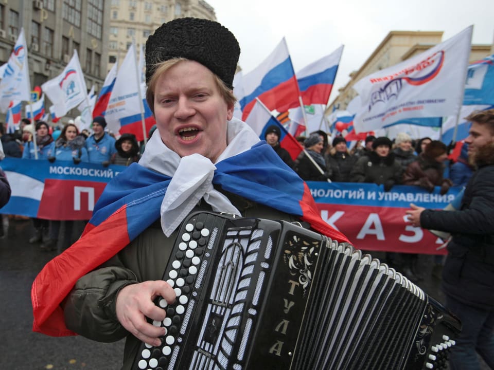 Mann in Russlandfahne gehüllt spielt Akkordeon.