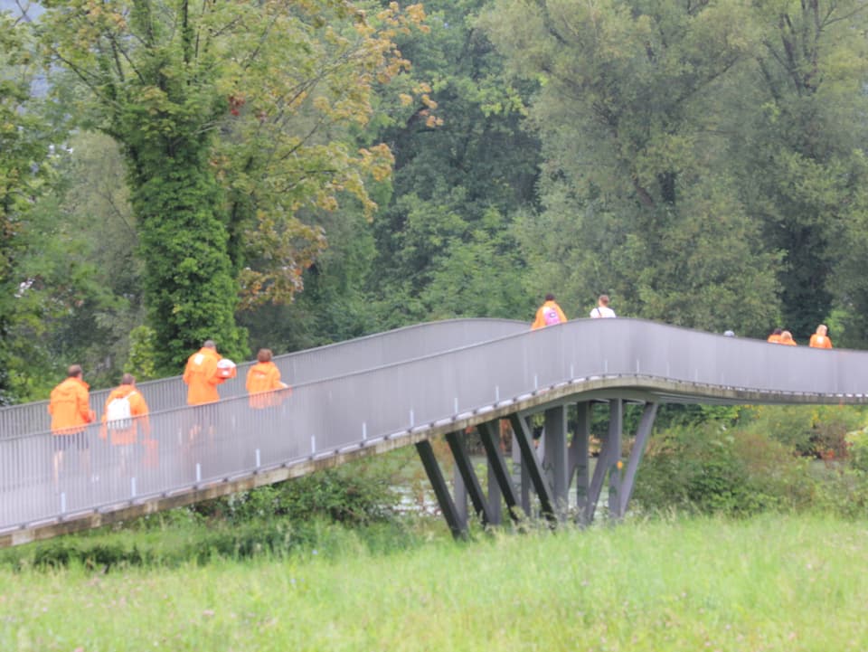 Radioleute in orangen Jacken laufen über eine Brücke.