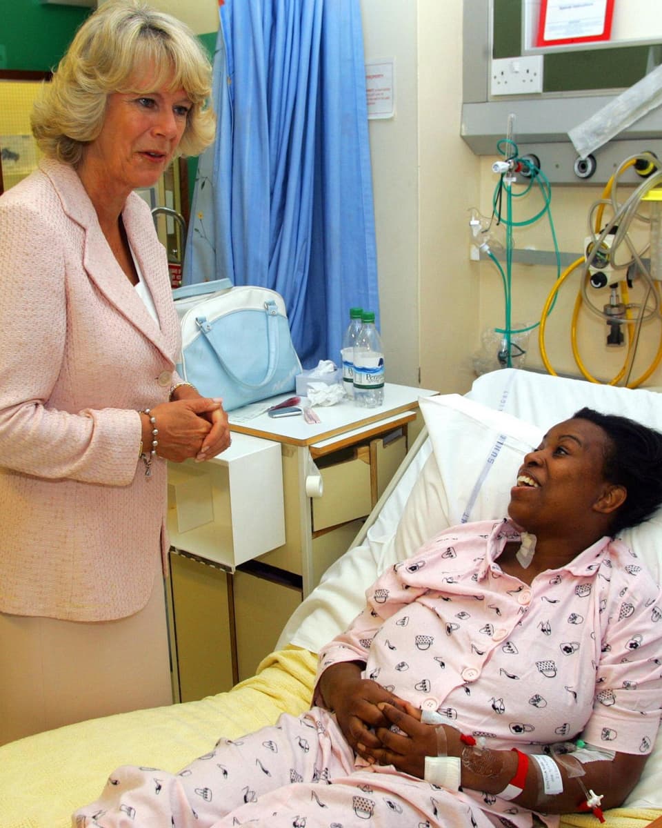 Camilla steht am Spitalbett einer dunkelhäutigen Frau