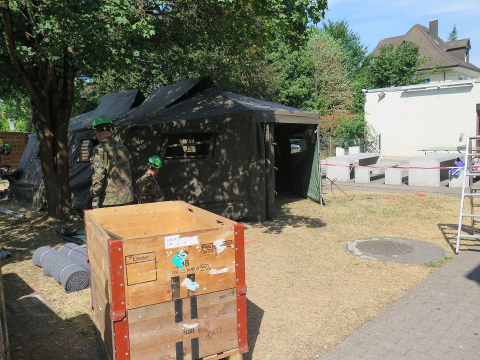 Holzkiste mit Material, im Hintergrund Zelte. 