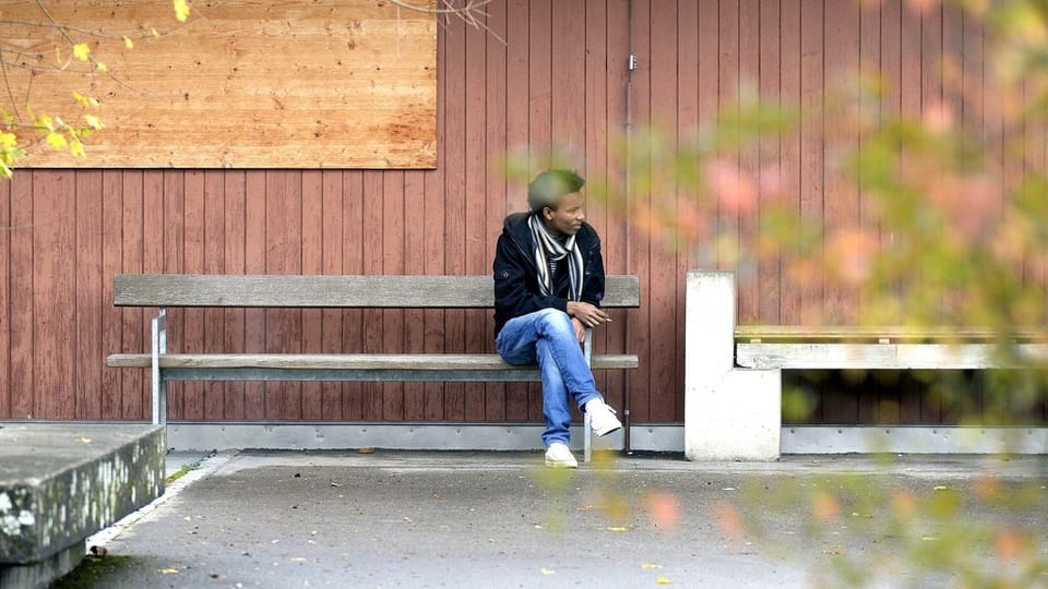 Asylbewerber sitzt in Bremgarten vor der Unterkunft auf einer Bank und raucht eine Zigarette, er wirkt gelangweilt.
