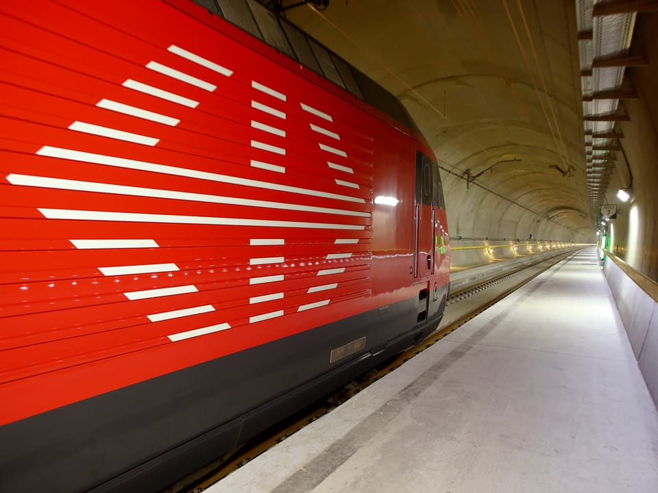 Blick in den 57-km-langen Gotthard-Basistunne, im Vordergrund eine rote Lok von der Seite. 