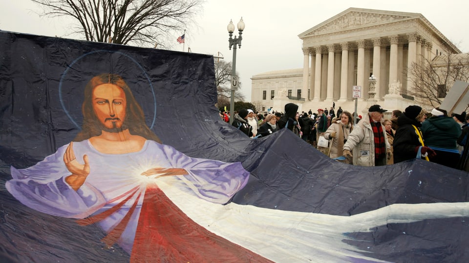 Demonstranten tragen ein grosses Tuch mit einer Jesusfigur. 