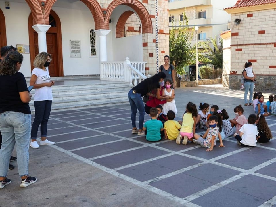 Schulkinder sitzen vor dem Schulhaus am Boden.