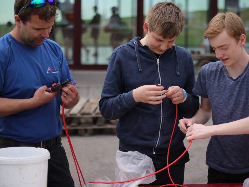 Konzentriert Arbeiten zwei Schüler und ein Fachmann mit Kabeln der Solaranlage.