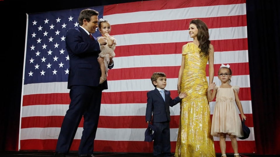 Ron DeSantis hat seine Tochter auf dem Arm. Seine Frau steht neben ihm, mit einem gelben Kleid, zwei weitere Kinder.