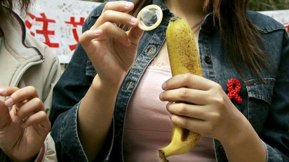 Junge Frau ist kurz davor, ein Kondom über eine Banane zu rollen.