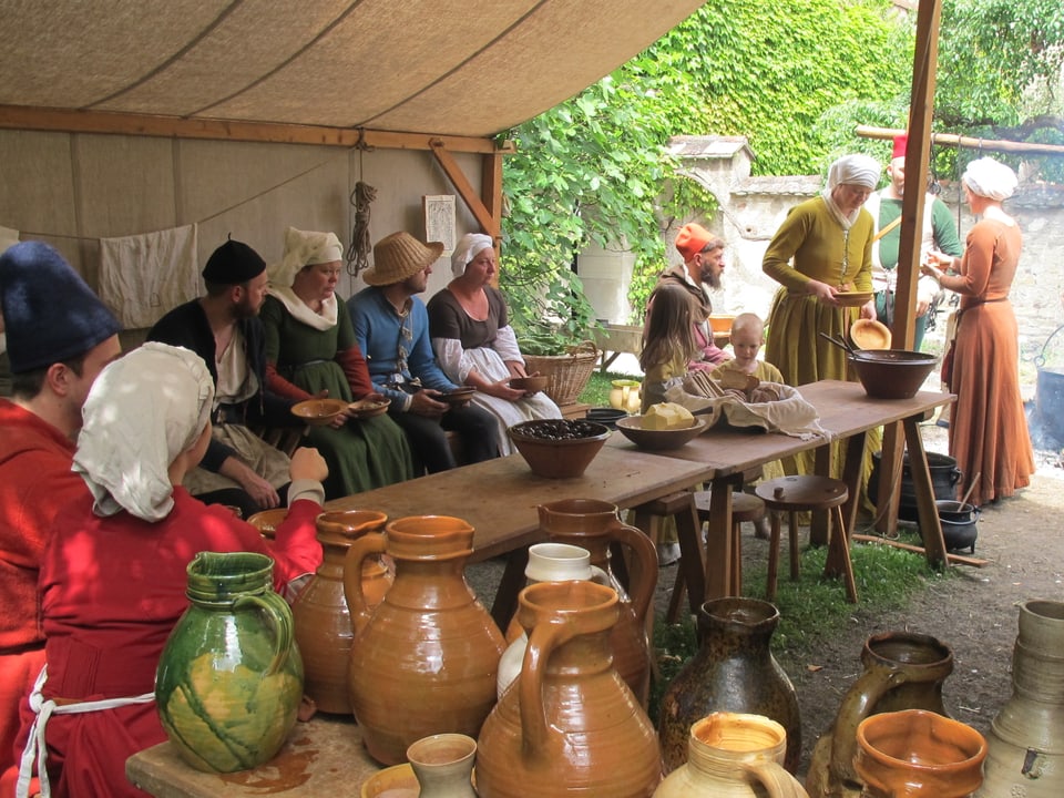 Leute in mittelalterlichen Kleidern beim Essen in einem Zelt.