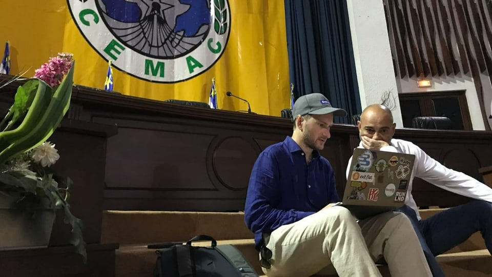 Zwei Männer mit Laptop sitzen in einem alten Konferenzraum