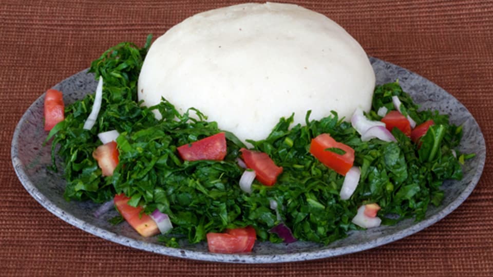 Auf einem Teller befindet sich weisser Ugali und grüner Spinat und Tomaten.