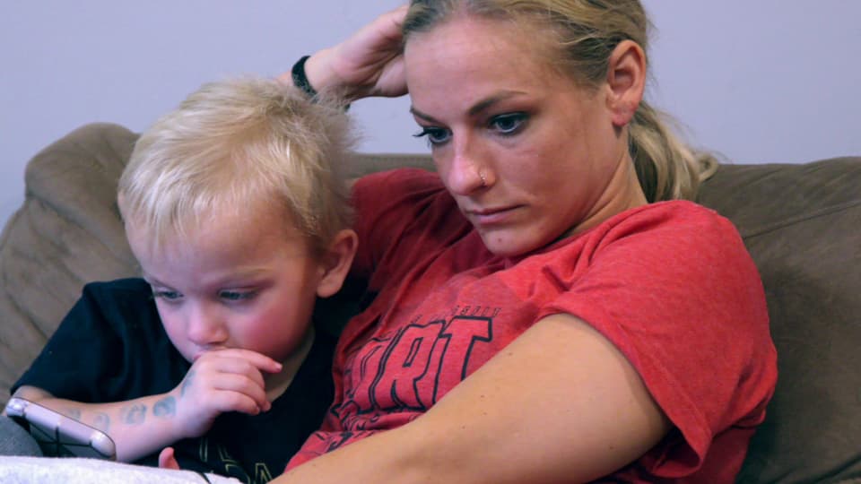 Eine junge, blonde Frau sitzt neben ihrem Kleinkind. Sie sieht gestresst aus.