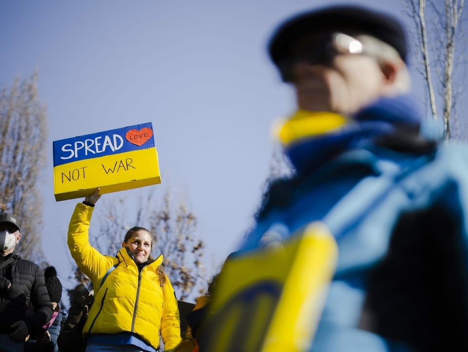 Person mit einem Plakat mit der Aufschrift «Spread Love – Not war».