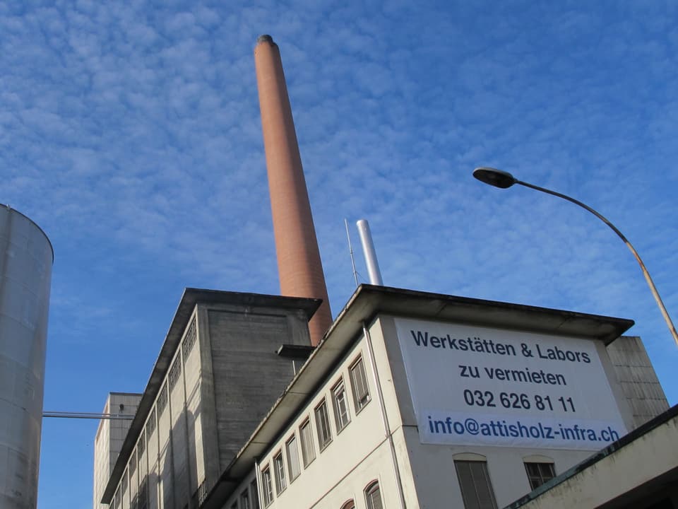 Blick auf ein Fabrikgebäude mit einem grossen Plakat, auf dem Mieter für das Areal gesucht werden.