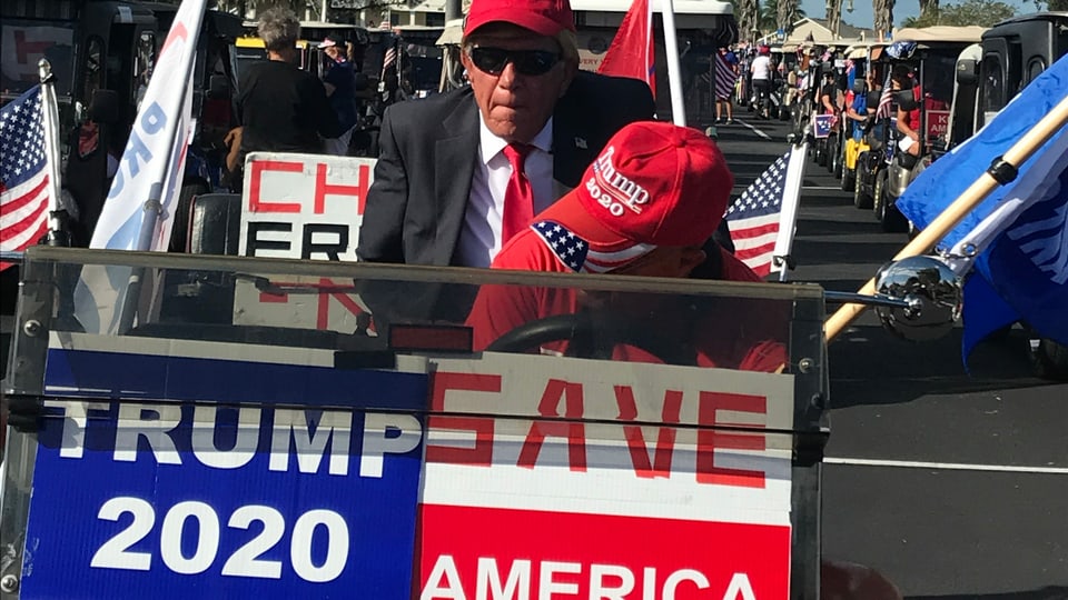 Ein als Donald Trump verkleideter Mann in einem Golfwagen mit Wahlplakaten.