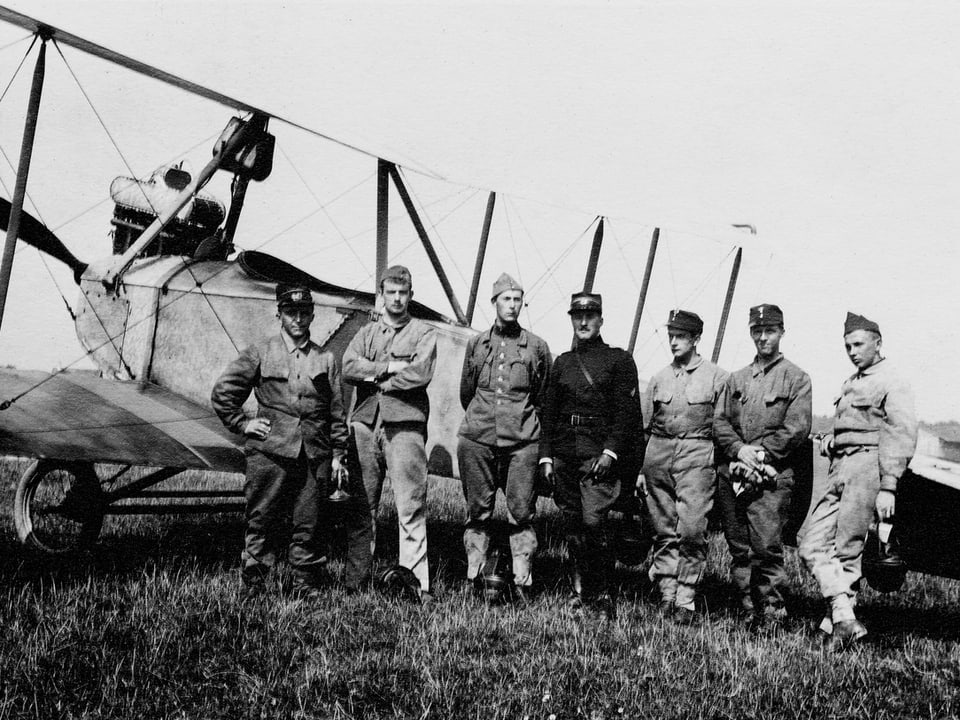 Eine alte Fotografie zeigt Männer vor einem Flugzeug.