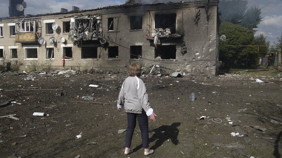 Frau steht vor einem stark beschädigten Gebäude nach einem Brand.