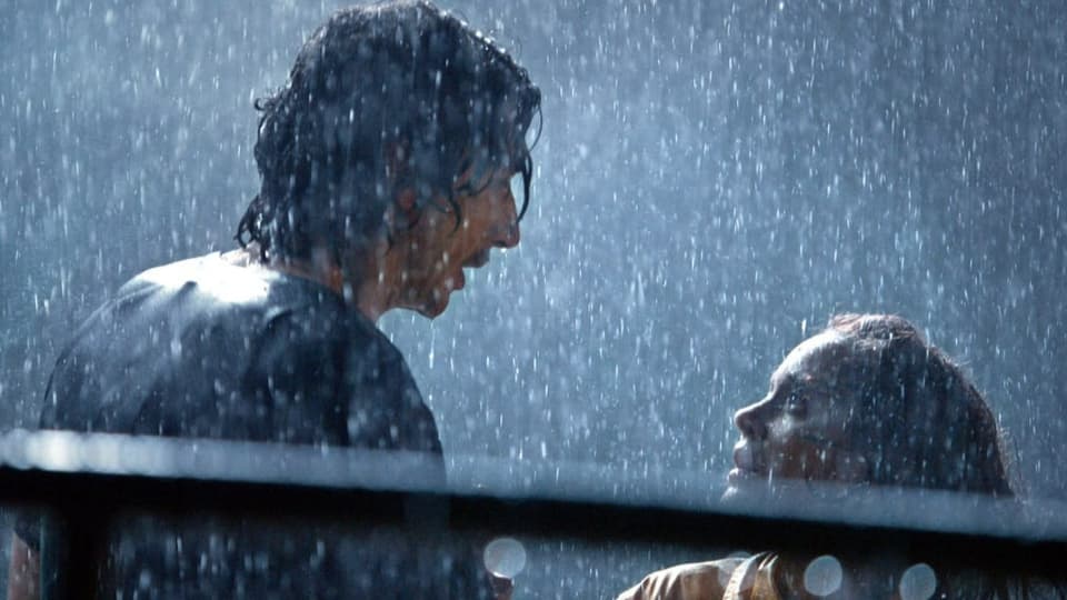 Ein Mann und eine Frau blicken sich in die Augen. Es regnet in Strömen.