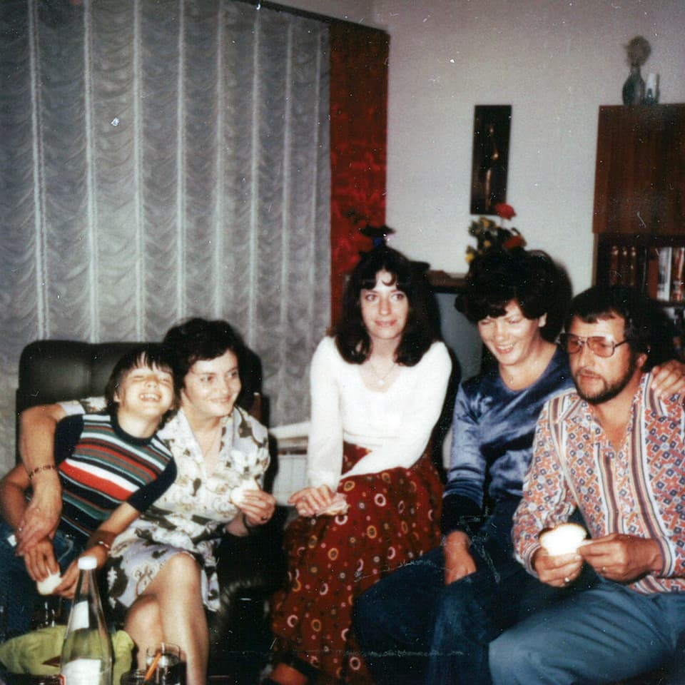 Drei Frauen, ein Mann und ein Bub sitzen in einem Wohnzimmer beieinander.
