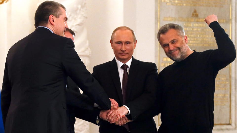 Drei Männer, darunter Wladimir Putin, geben sich die Hände. Der Mann rechts im Bild streckt die Faust in die Höhe.