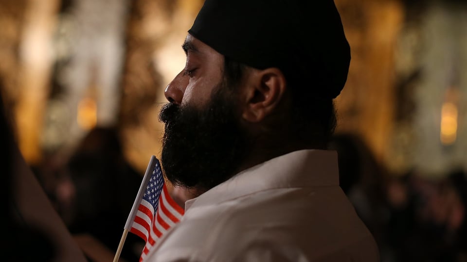 Ein Mann mit einem Turban hält eine amerikanische Flagge.