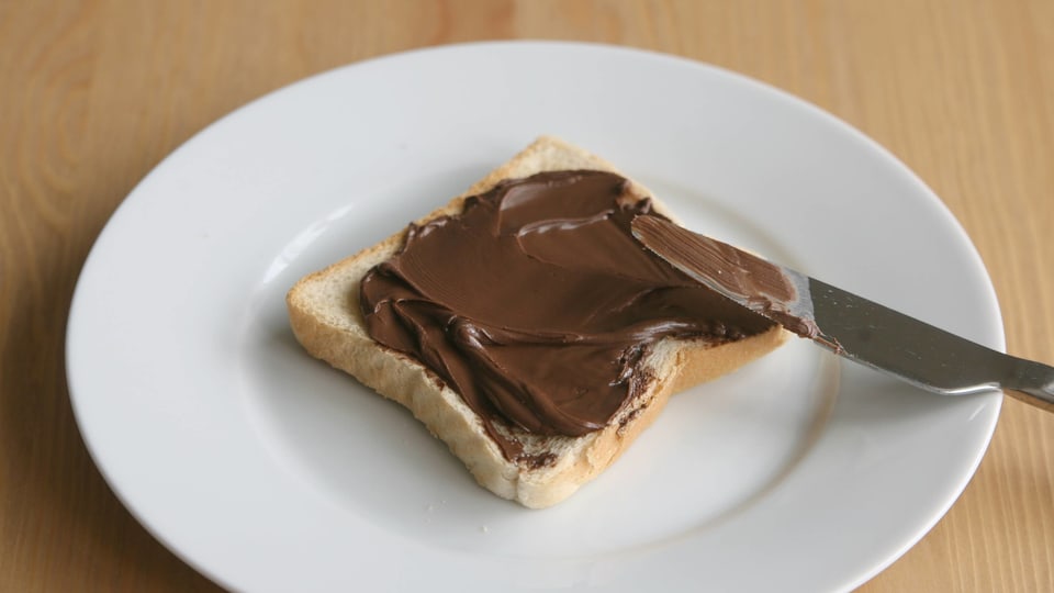 Ein mit Nutella bestrichener Toast liegt auf einem weissen Teller. 