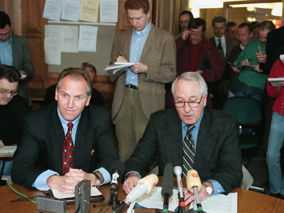Zwei Personen sitzen an einem Tisch mit Mikrofonen.