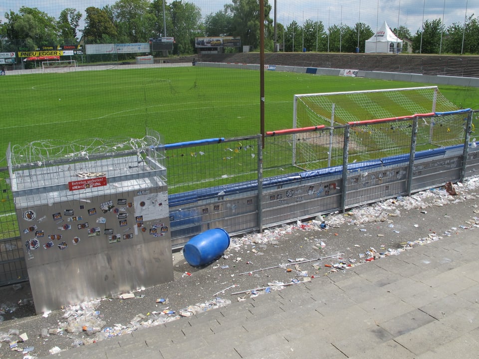 Blick auf das Spielfeld, im Vordergrund Abfall und zerrissene Gitter