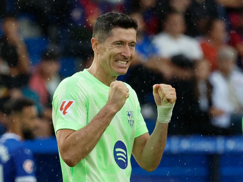 Jogador de futebol em camisa verde comemora na chuva.
