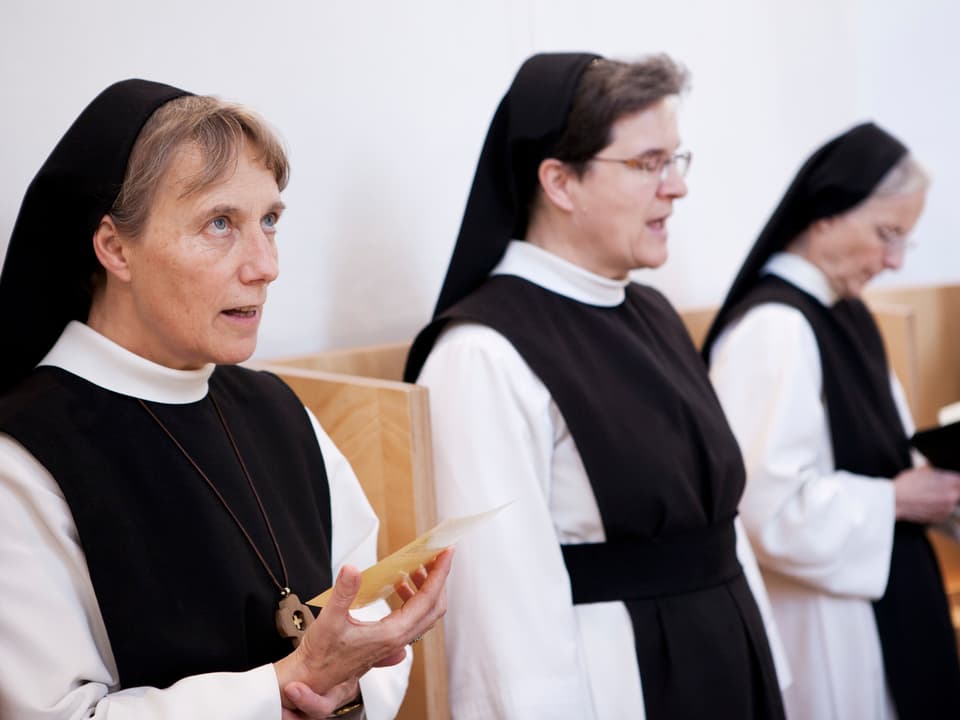 Drei Nonnen sind in einem Chorgestühl am Singen. 