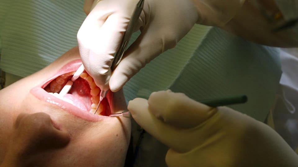 Ein Mund einer Frau und darin Zahnarzt-Werkzeuge.