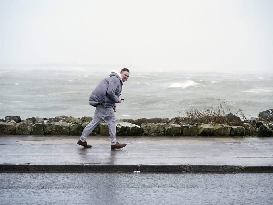 Ein Mann kämpft auf dem Strandweg gegen den Wind an.