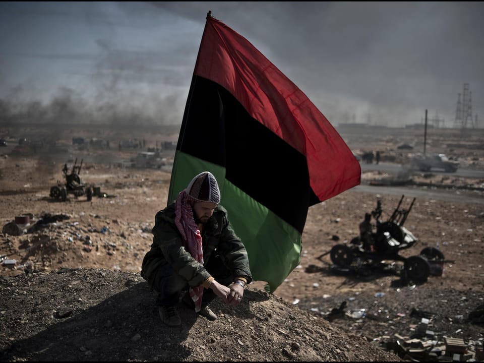 Lybischer Aufständischer im Kriegsgebiet kauert vor seiner Fahne,