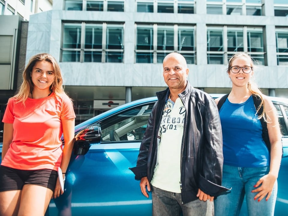 Ein Mann mit seinen beiden Töchter vor einem blauen Auto
