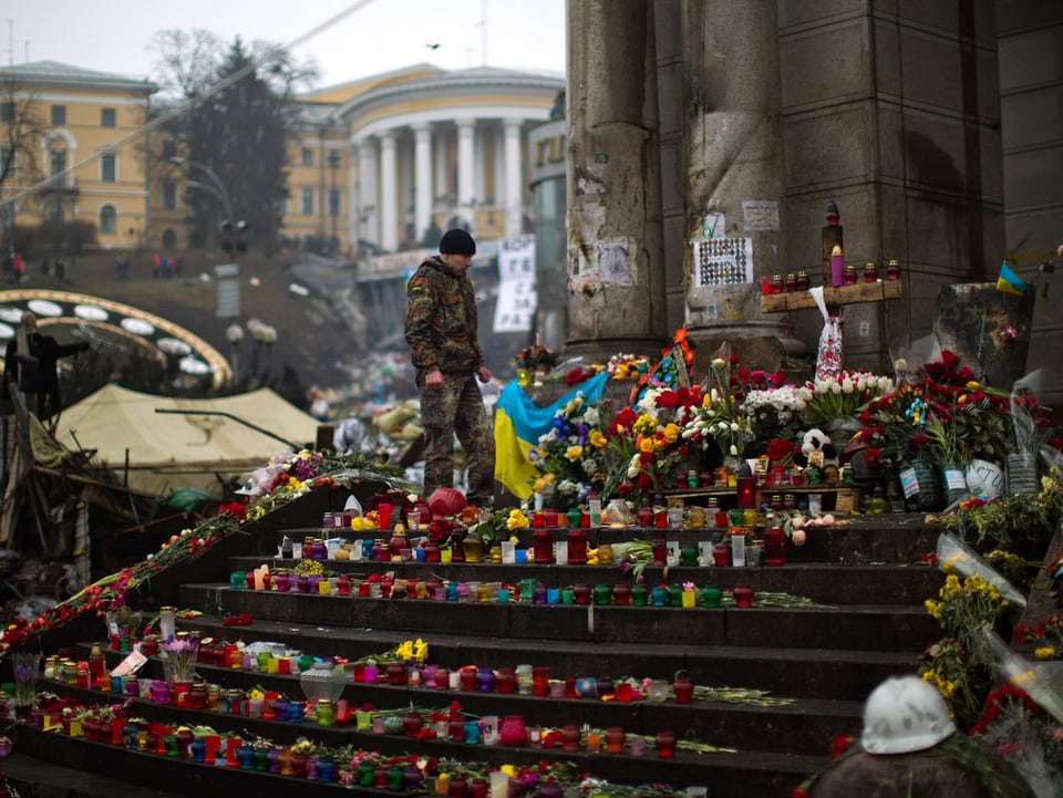 Unzählige Blumen und Kerzen liegen auf der Treppe beim Unabhängigkeitsplatz, ein Soldat steht dazwischen.