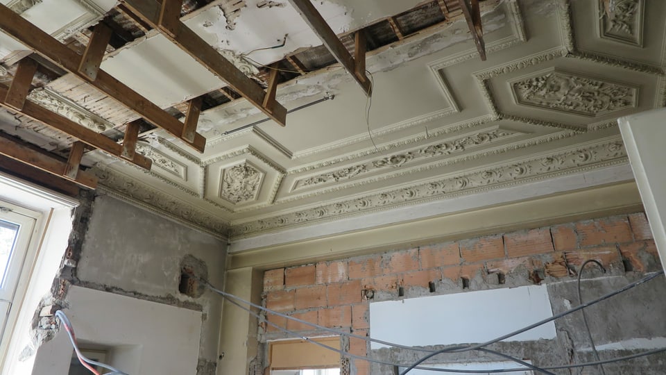 Aufnahme aus dem Innenraum der Villa: Stuckdecke, zum Teil zerstört, offene Wände mit heraushängenden Elektroleitungen