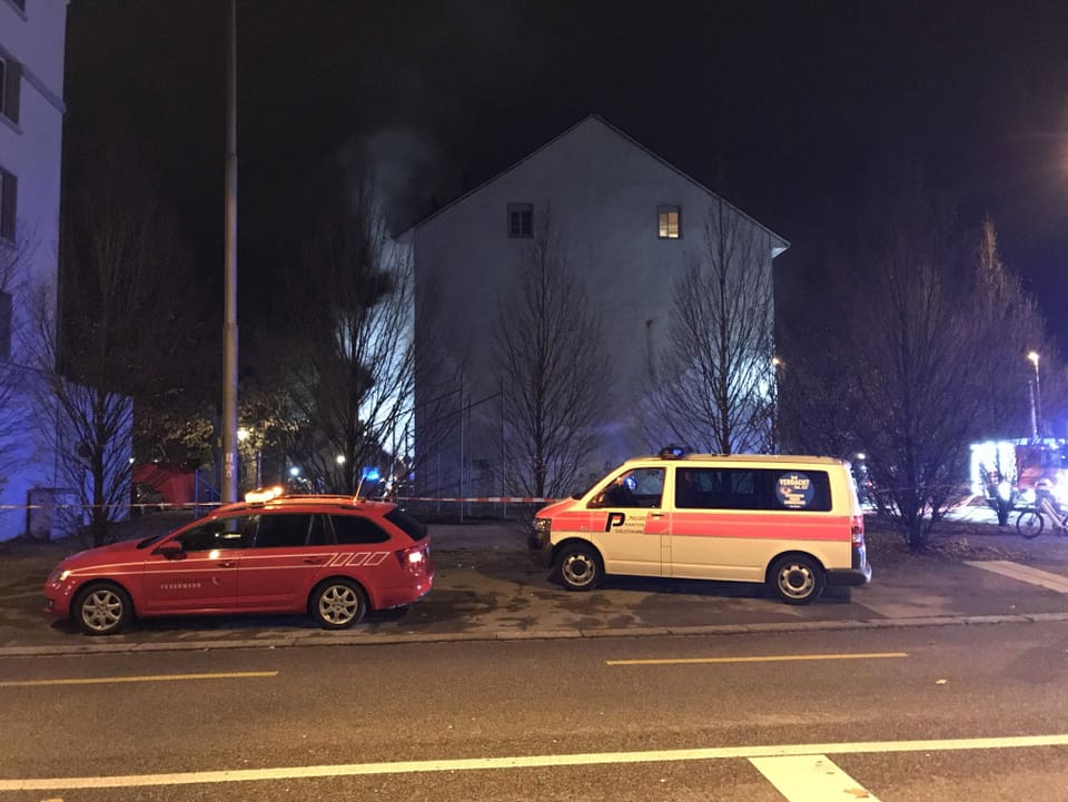 Zwei Polizeiautos stehen neben brennendem Wohnhaus. 