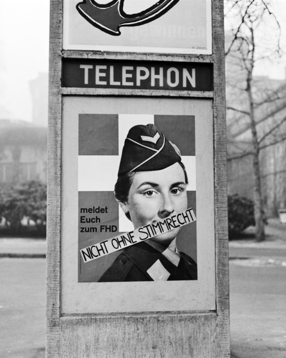 Schwarz-weiss-Bild eines Werbeplakats auf das ein Spruchband aufgeklebt ist. Darauf steht: «Nicht ohne mein Stimmrecht»