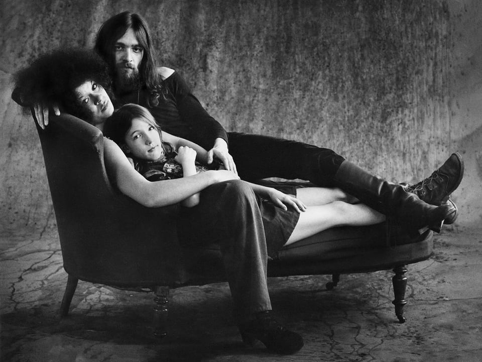 Schwarzweiss-Bild: Eine Hippie-Familie auf einem Sofa.