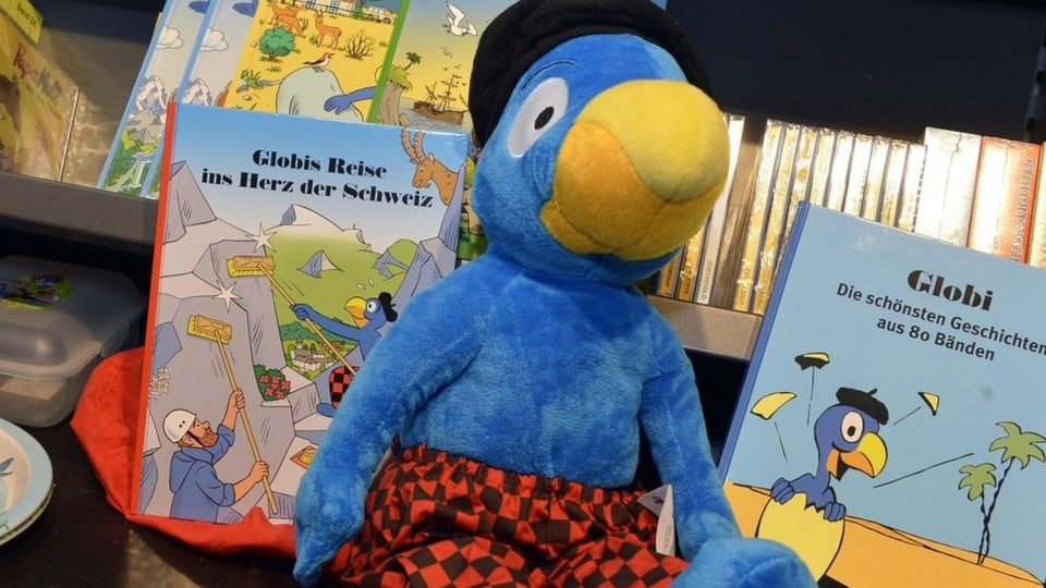 Ein blauer Plüschvogel vor einer Auslage von Büchern.