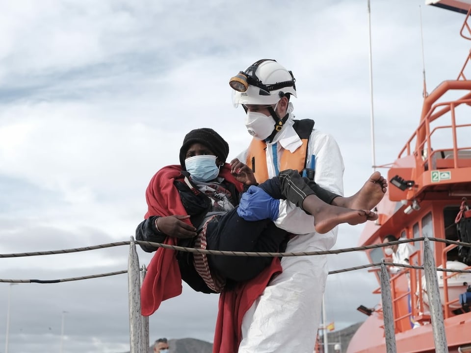 Migrant wird von Helfer von einem Rettungsboot getragen