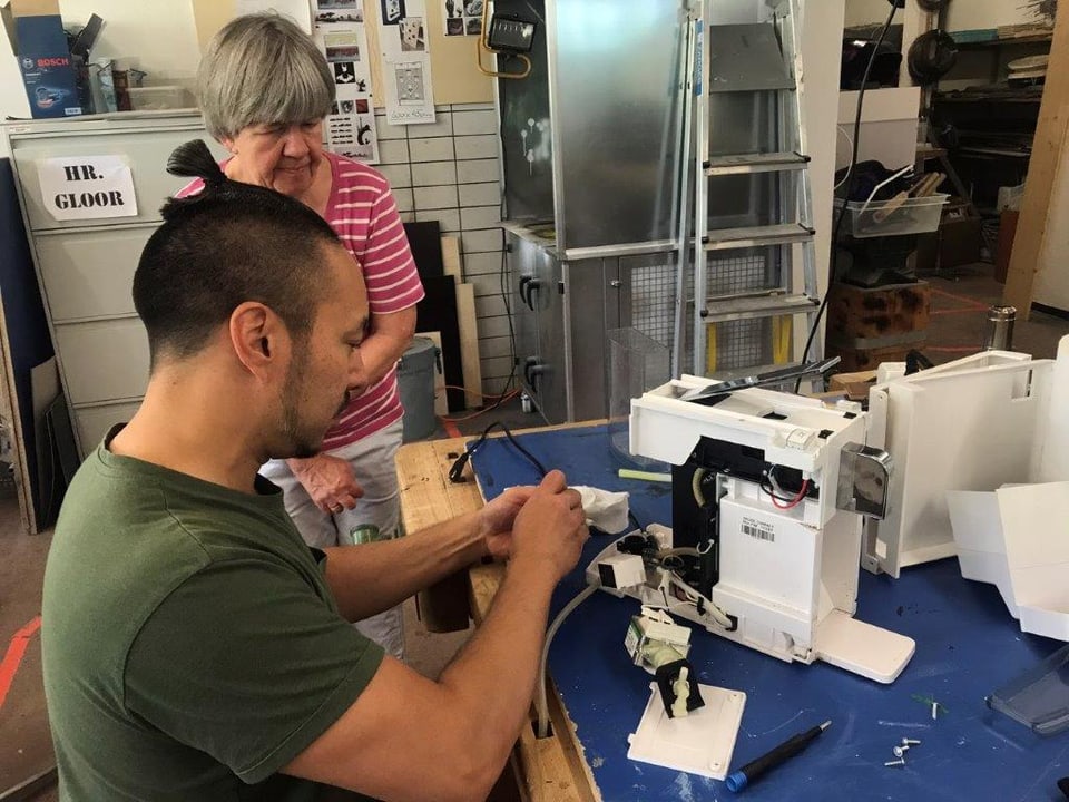 Eine Frau schaut einem Mann zu, wie er eine Nähmaschine repariert.
