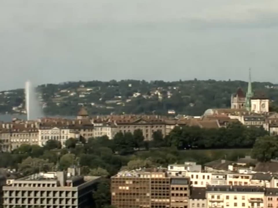 Genf mit dem Jet d'eau, der Kathedrale und Segelschiffen auf dem See. Der Himmel ist mit einem feinen Schleier von hohen Wolken überzogen.