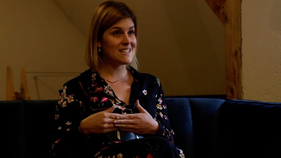 Tanja Herrmann Tanja Herrmann sitzt auf einem Sofa. Sie schaut ernst und gestikuliert mit ihren Händen.