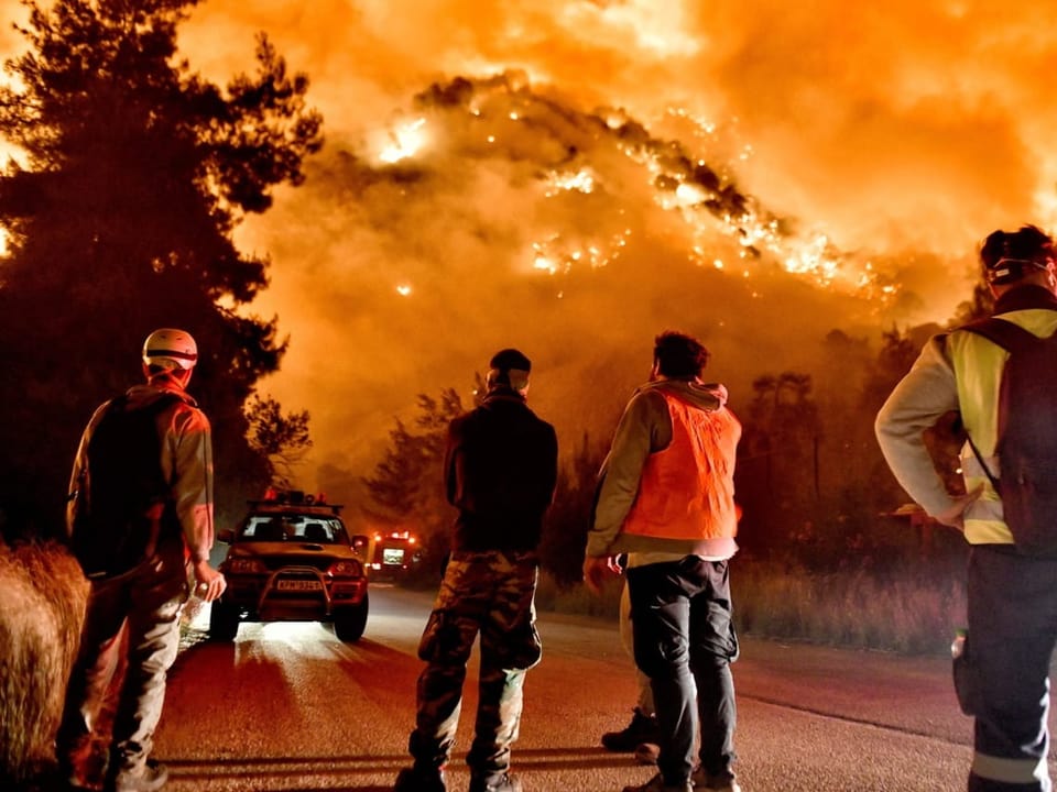 Feuerwehrleute schauen auf einen brennenden Hügel