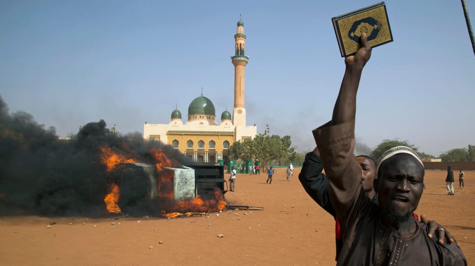 Ein Mann hält neben einem brennenden Auto vor einer Moschee in Niamey einen Koran in die Höhe. (reuters)