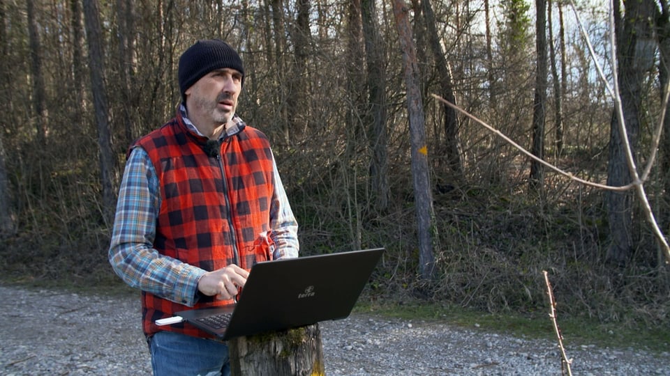 Ein Mann steht mit Laptop im Wald.