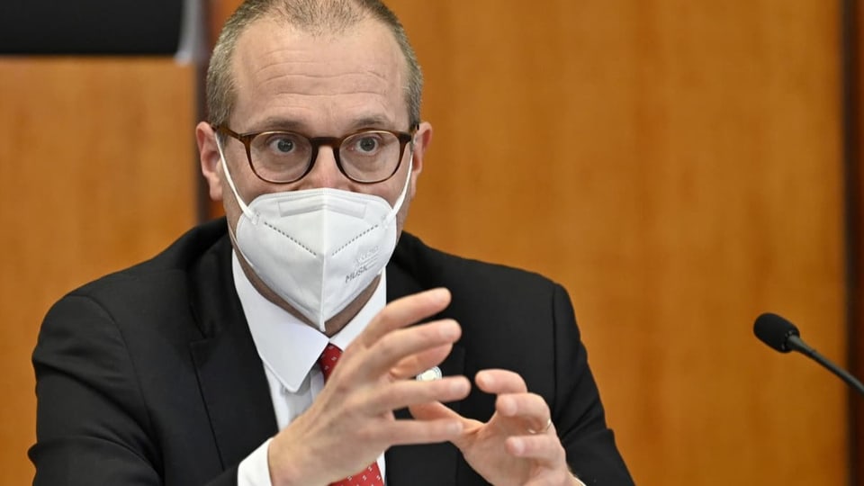 Ein Mann gestikuliert, trägt eine Schutzmaske im Gesicht und trägt eine Brille.